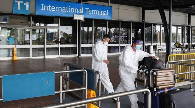 يغادر المسافرون في معدات الحماية الشخصية المحطة الدولية لموقف سيارات الأجرة في مطار سيدني ، حيث تتفاعل الدول مع البديل الجديد لفيروس كورونا أوميكرون