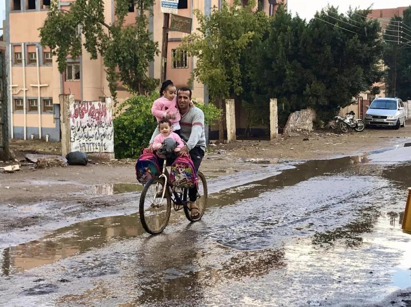 رجل يحمل أطفاله على دراجة نارية تحت المطر